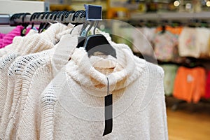 Stylish clothes on hangers in the store, white sweaters