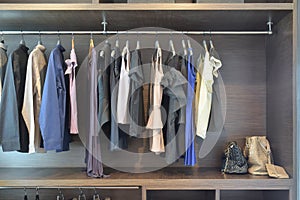 Stylish cloths in dark shade hanging in open wooden wardrobe