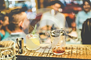 Stylish cocktails on american bar counter with people having fun in background - Vintage pub view at night time - Party trends,