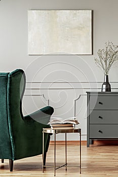 Stylish coffee table next to emerald green armchair in trendy living room interior with grey design