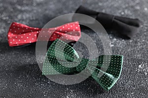 Stylish color bow ties on black textured background, closeup