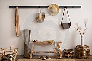 The stylish composition of cosy entryway with wooden basket, carpet, hanger and personal accessories. Beige wall. Home decor.