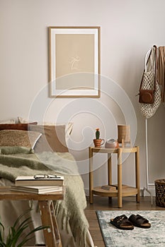 Stylish composition of cozy bedroom with mock up, beige bedding, and wooden coffee table. Mock up poster with wooden frame. Home