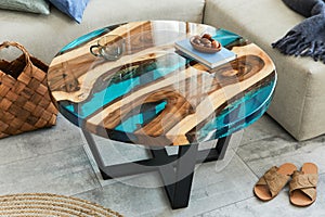 Stylish composition with design epoxy coffee table, sofa, blanket, pillows, book, decoration and personal accessories.