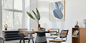 Stylish composition of dining room interior with design table, modern chairs, decoration, tropical leaf in vase, fruits.