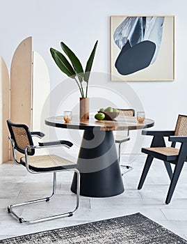 Stylish composition of dining room interior with design table, modern chairs, decoration, tropical leaf in vase, fruits.