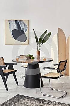 Stylish composition of dining room interior with design table, modern chairs, decoration, tropical leaf in vase, fruits, carpet.