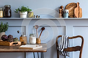 Stylish composition of kitchen interior with wooden family table, chairs, vegetables, herbs, plants, fruits, food supplies.