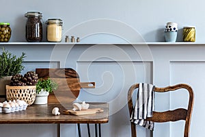 Stylish composition of kitchen interior with wooden family table, chairs, vegetables, herbs, plants, fruits, food supplies.