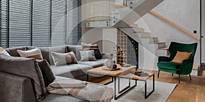 Stylish composition of living room interior with corner grey sofa, green velvet armchair, coffee table, wooden floor, design