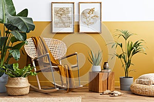 Stylish composition of living room interior with design rattan armchair, two mock up poster frames, plants, cube.