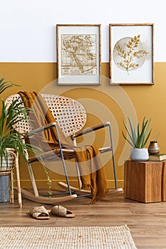 Stylish composition of living room interior with design rattan armchair, two mock up poster frames, plants, cube.