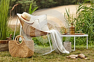 Stylish composition of outdoor garden on the lake with design rattan armchair, coffee table, plaid, pillows, drinks and elegant ac