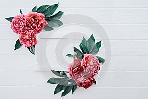 Stylish composition with photo frame with blank canvas and red pink peony flowers with green leaves on the white wooden background