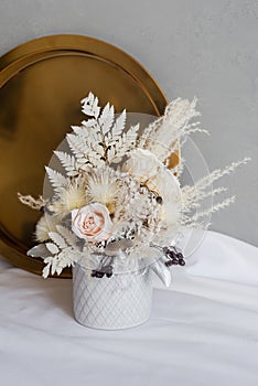 Stylish composition of preserved flowers and dried flowers in a light color scheme on the background of a golden tray.