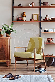 Stylish composition of retro living room interior with design armchair, wooden bookcase, picture frames, plant, carpet, slippers.