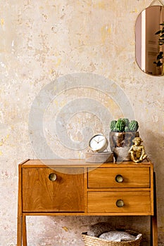 Stylish composition of retro living room interior with wooden vintage commode, gold pink mirror, plant, rattan basket, plaid.