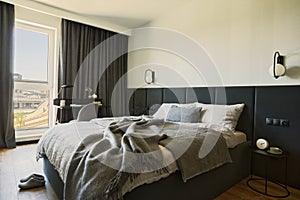 Stylish composition of small modern bedroom interior. Bed, creative lamp and elegant personal accessories.Walls with black panels.