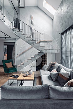 Stylish composition with stairs in living room interior. Grey sofa, green velvet armchair, coffee table and minimalist personal