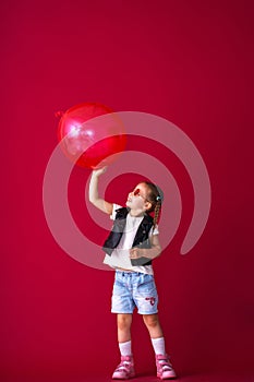 stylish and cool little girl in sunglasses, leather vest playing big red balloon