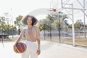 Stylish cool teen girl gathering at basketball court, playing basketball outdoors