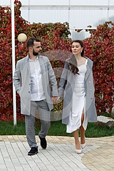 Stylish couple in gray coats walking in the autumn park. Happy sensual wedding couple. Romantic moments of newlyweds