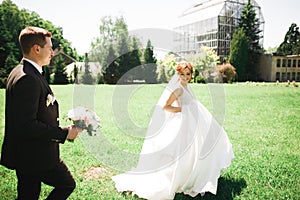 Stylish couple of happy newlyweds. Bride running from groom in the park on their wedding day with bouquet