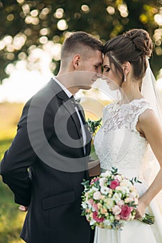 Stylish couple of happy newlyweds walking in field on their wedding day with bouquet. In the middle of the field ther is