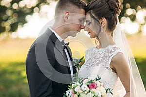 Stylish couple of happy newlyweds walking in field on their wedding day with bouquet. In the middle of the field ther is