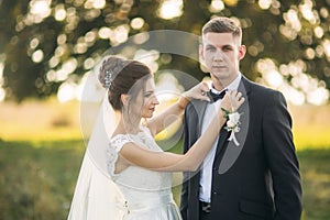 Stylish couple of happy newlyweds walking in field on their wedding day with bouquet. In the middle of the field ther is