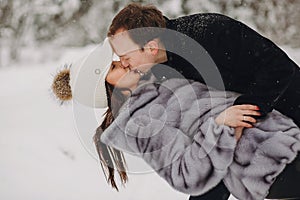 Stylish couple in love gently kissing in snowy mountains. Portraits of happy family gently embracing and smiling in winter