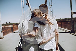 Stylish couple in love hugging, back view with windy hair, on br