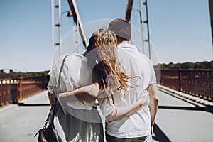 Stylish couple in love hugging, back view with windy hair, on br