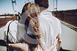 Stylish couple in love hugging, back view with windy hair, on br