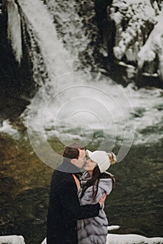 Stylish couple in love kissing in winter snowy mountains. Happy