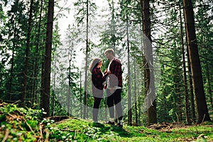 Stylish couple of men and women in red shirts on a hike stopped to rest in a coniferous forest  standing on the moss against the