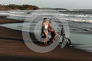 Stylish couple on a motorbike by the sea. Couple in love at sunset by the sea. Beautiful couple on a bike. Travel on a motorbike.