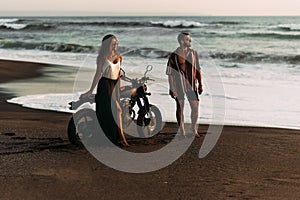 Stylish couple on a motorcycle on the beach. A couple on a motorcycle meets the sunset. Beautiful couple on a motorcycle.