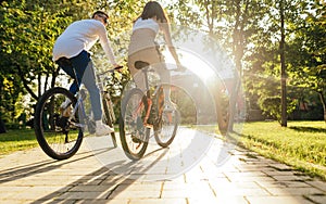 Stylish couple riding bicycles in autumn park at sunset. Man and woman ride a bike along the alley in the park. Back view