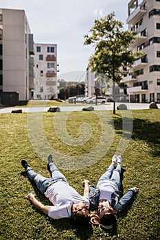 Stylish couple smiling and look at each other lying on green grass