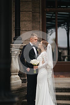 Stylish couple stand on the stairs by the palace. Handsome groom and gogeous bride at the wedding