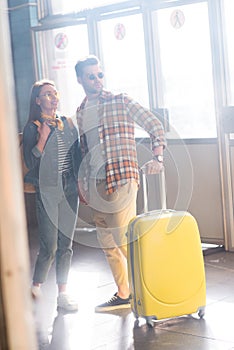 stylish couple of tourists in sunglasses with backpack and wheeled bag