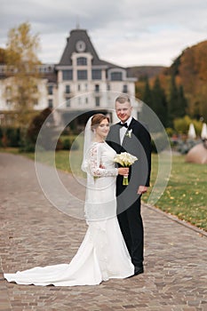 Stylish couple walking in the park at their wedding day. Happy newlyweds outside in autumn weather. Background of yellow