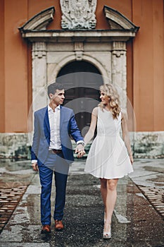 Stylish couple walking together in european city street on background of old architecture. Fashionable bride and groom in love