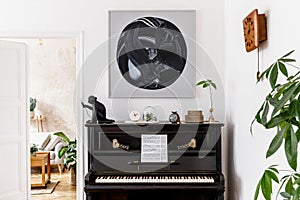 Stylish and cozy interior of living room with black piano, furniture, plant, wooden clock, lamp, mock up painitngs, carpet.