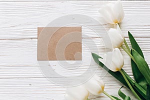 Stylish craft greeting card and tulips on white wooden rustic ba