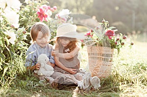 Stylish cute children boy and girl sit near peonies flowers photo