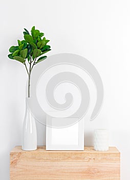 Stylish decor with white picture frame, ficus leaves and candle