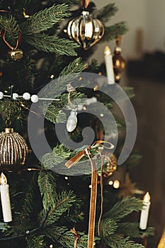 Stylish decorated christmas tree with vintage baubles, ribbons, candles and golden lights. Atmospheric winter holiday time.