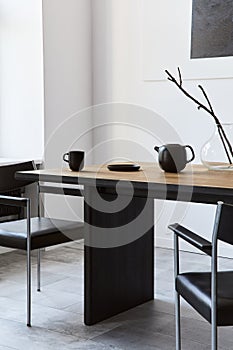 Stylish dining room interior with design wooden family table, black chairs, teapot with mug, mock up art paintings on the wall.